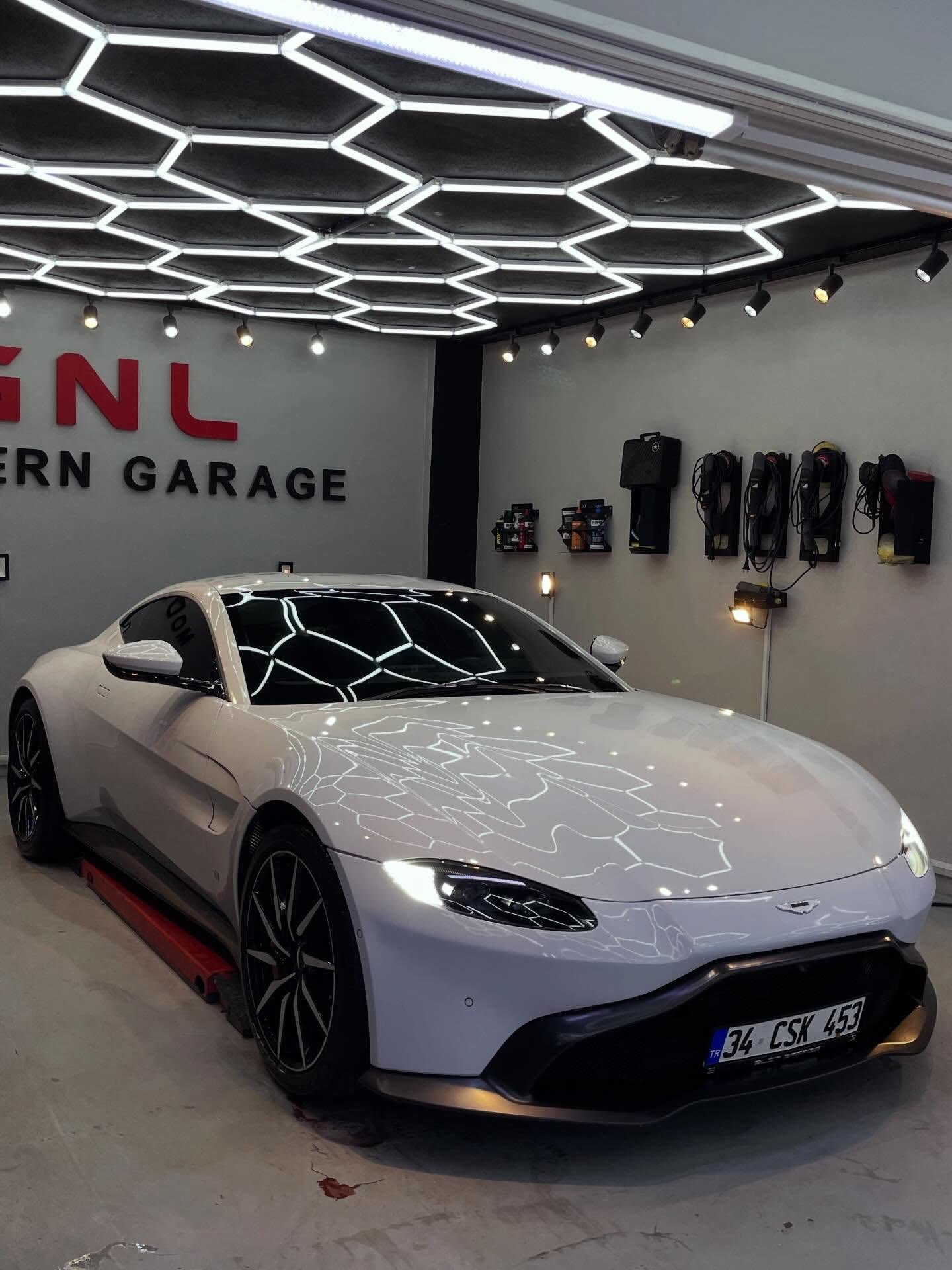 GNL Modern Garage atölyesinde beyaz Aston Martin Vantage, altıgen tavan aydınlatması altında
